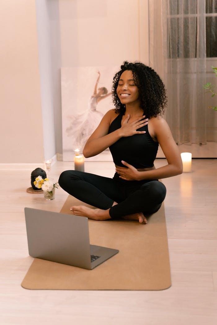 African American woman practicing yoga and meditation indoors with a laptop.